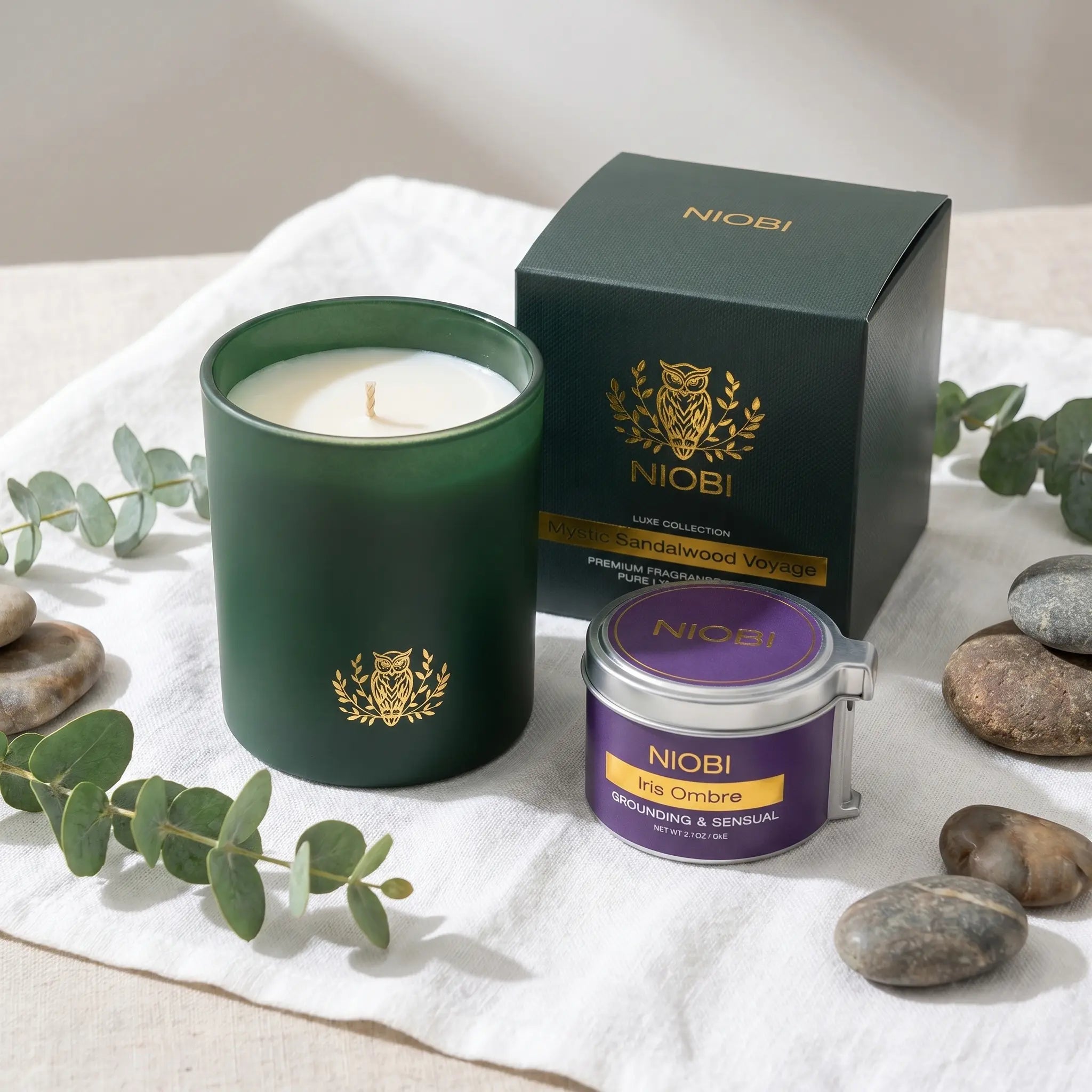 NIOBI СПА у дома ароматна свещ Mystic Sandalwood Voyage с кутия и масажна свещ Iris Ombre върху ленена кърпа с евкалипт и спа камъни